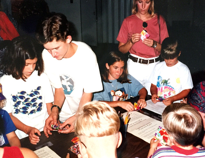 Children gathered around a table fold brightly colored paper.